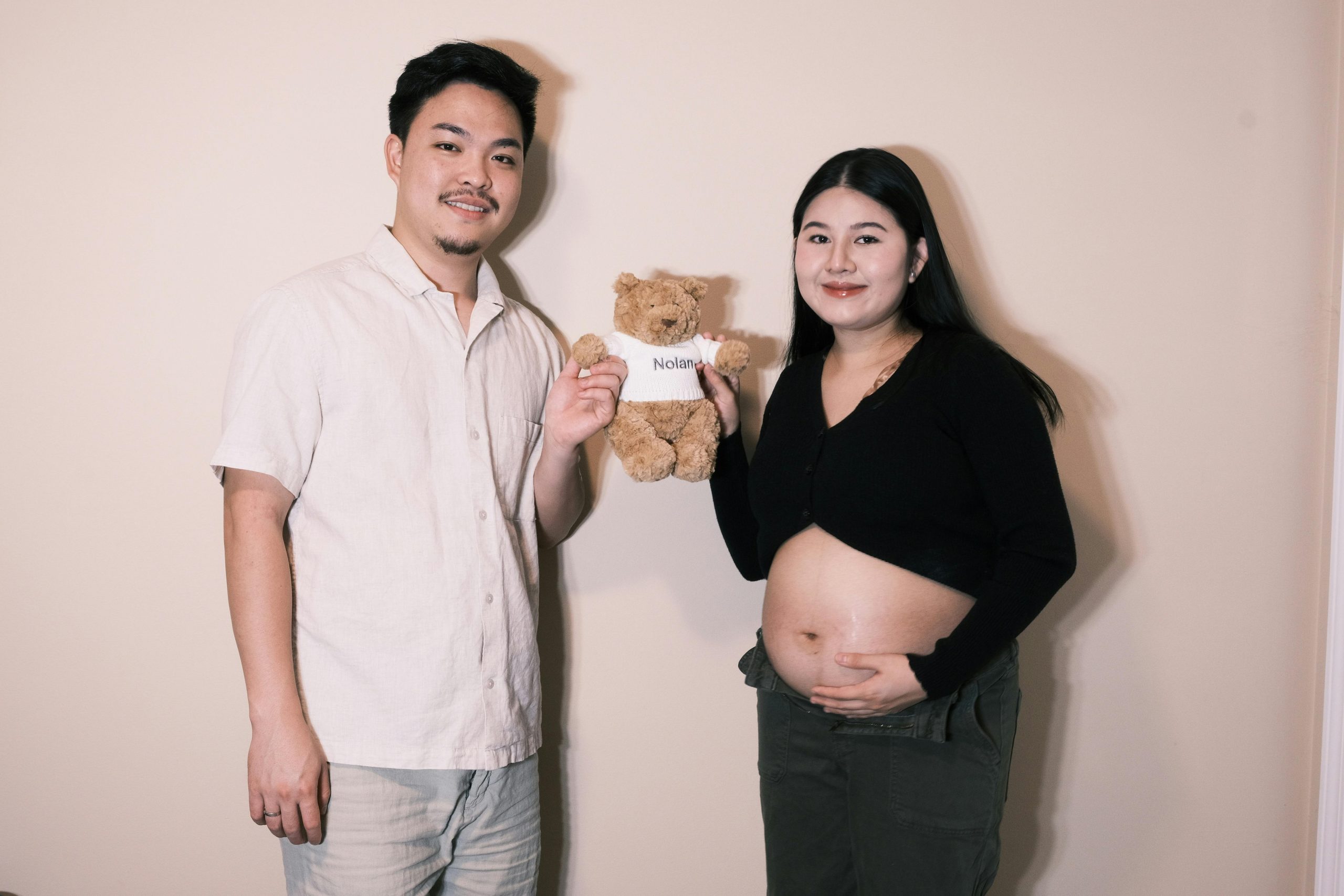 expectant father and pregnant woman holding a teddy bear together between them