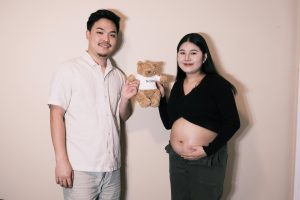expectant father and pregnant woman holding a teddy bear together between them