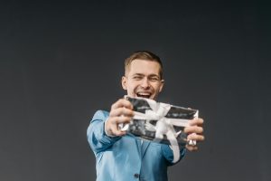 man in a powder blue blazer holding out a gift wrapped in silver paper with a white ribbon