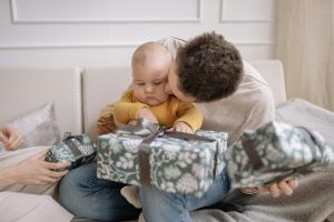dad kissing his baby while the baby tries to untie a ribbon on a gift box